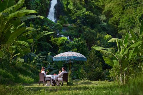 Dos personas sentadas en una mesa bajo una sombrilla frente a una cascada. en The Sira, a Luxury Collection Resort and Spa, Lombok, en Tanjung