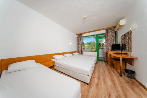 two beds in a room with a desk and a television at Hotel Zdravets in Varna City