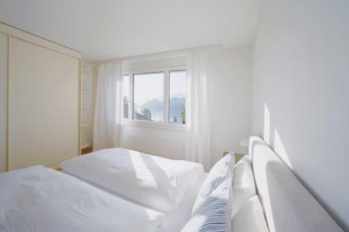 a white bedroom with two beds and a window at Traumhafte 4,5-Zi-Wohnung mit Sicht auf den See in Alpnach