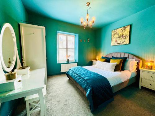 a blue bedroom with a bed and a desk and a mirror at HomeDecor Cottages - Castle Walk House in Alnwick