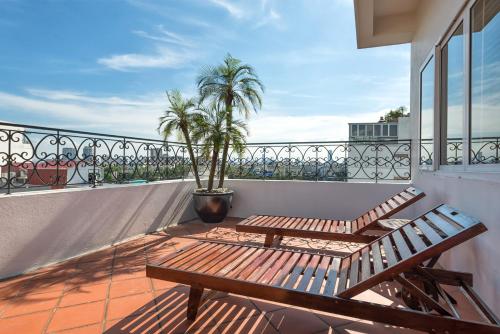 einen Balkon mit zwei Holzbänken und einer Palme in der Unterkunft Hanoi E Central Luxury Hotel & Restaurant in Hanoi