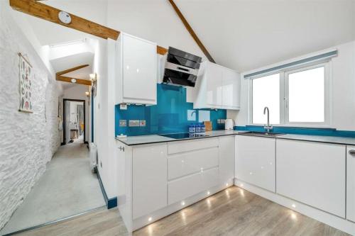 una cocina con armarios blancos y detalles azules en Beautiful Quayside Cottage Looe, en Looe