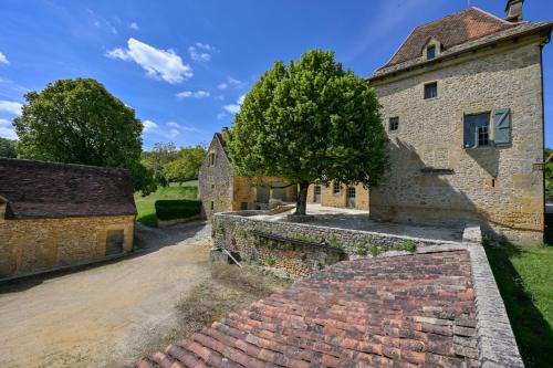 an old stone building with a tree in front of it at Le Mayne in Beynac-et-Cazenac