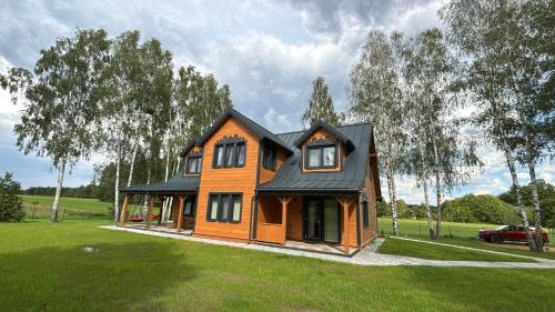 a house with a black roof on a green field at Żubrowe Sioło - dom w naturze - najładniejsze widoki - nowość in Białowieża