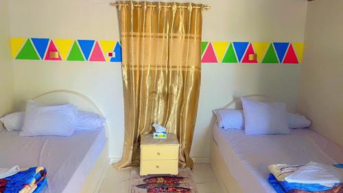 two twin beds in a room with a colorful curtain at Wateen guest house in Jazīrat Aswān