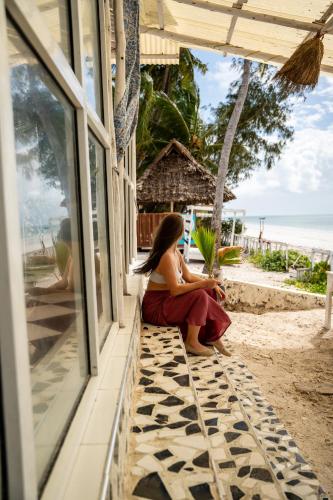 a woman sitting on the porch of a beach house at ZAN Orient Beach Hotel in Bwejuu