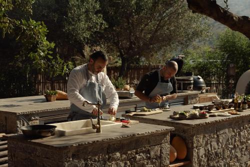 two men in a kitchen preparing food on a table at Phāea Blue - Small Luxury Hotels of the World in Elounda