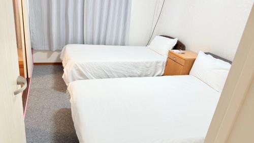 two beds in a hotel room with white sheets at 瀬戸内多賀町201 in Kusukamimachi