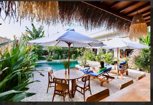 a woman sitting in a chair under an umbrella next to a pool at Villa AmoreMia in Gili Trawangan