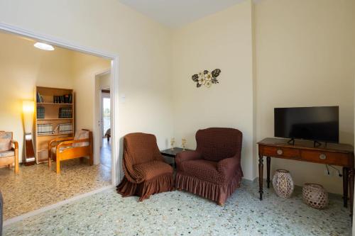 a living room with two chairs and a table and a television at Valira Stathmos Home, Rustic Charm Cottage w Views in Valíra