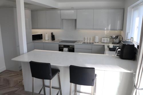 a kitchen with a white counter and two bar stools at Amora Stays in Buckinghamshire