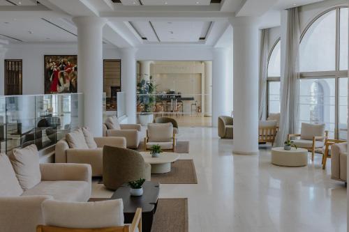 a lobby with white couches and tables and windows at Golden Coast Beach Hotel in Protaras