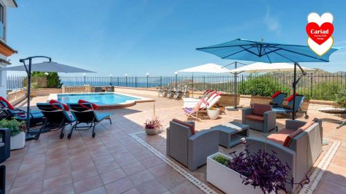 a patio with chairs and a swimming pool and an umbrella at Cariad Boutique Bed & Breakfast in Cala del Moral