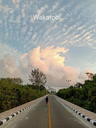 a person walking down a road with a cloudy sky at Wambuliga Homestay in Waha