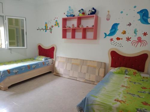 a bedroom with two beds and a window and a shelf at Dar lekhle3a in Kelibia