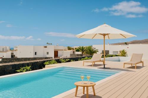 Una piscina con una sombrilla y dos vasos en una terraza. en Villa Ainé Luxury Villa, en Puerto Calero