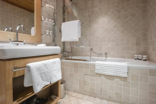 a bathroom with a tub and a sink and towels at Les Trois Vallées, a Beaumier hotel in Courchevel