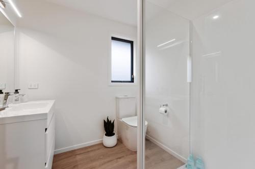 La salle de bains blanche est pourvue de toilettes et d'une douche en verre. dans l'établissement Lake McKay Escape, à Wanaka
