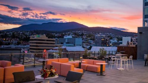 a rooftop patio with couches and tables and a sunset at Crowne Plaza Hobart by IHG in Hobart