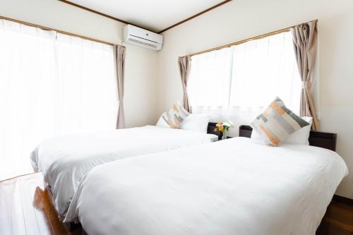 two white beds in a room with windows at エアポートサイドOmura in Omura