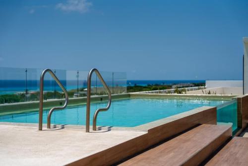 a swimming pool with metal hand rails next to the ocean at 2BR Condo w/ Rooftop Oceanview & Centric Location in Playa del Carmen