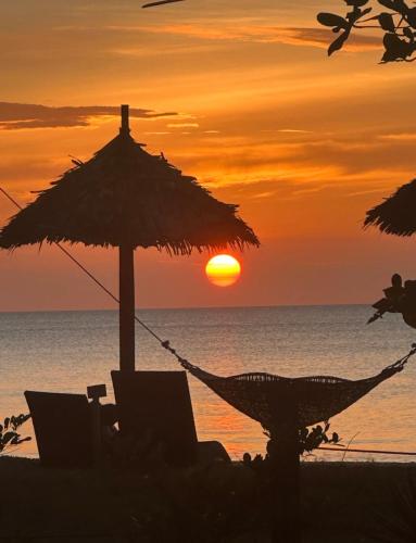 a hammock and an umbrella on a beach with the sunset at Eco Sanctuaries Nature Lodge Nacpan Beach, El Nido in El Nido