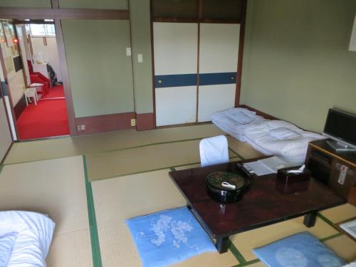 Zimmer mit 2 Betten, einem Tisch und einem Spiegel in der Unterkunft Komecho Ryokan in Imabari