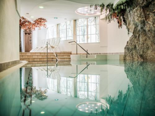 una piscina de agua en una habitación con escaleras y ventanas en Hotel Alpenjuwel en Melago