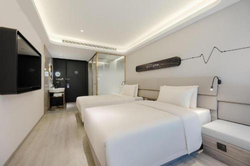 a white bedroom with two beds and a television at Atour X Hotel Qingdao Shilaoren Beach Exhibition Center Metro Station in Qingdao