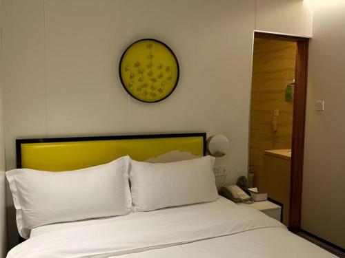 a bed with white pillows and a clock on the wall at Golden Central Hotel Shenzhen in Shenzhen