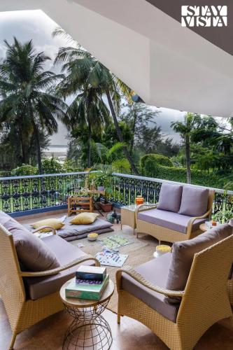 a living room with couches and a balcony with palm trees at StayVista at Waves by the Beach with Beach Access, Pool, Lawn in Alibag