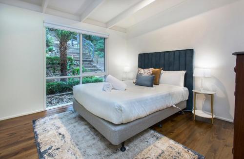 une chambre avec un grand lit avec une grande fenêtre dans l'établissement Belle Cottage Secluded Stay Near Shops Cafes, à Sassafras