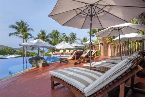 a group of lounge chairs with umbrellas next to a pool at Hilton Grand Vacations Club Zihuatanejo in Zihuatanejo