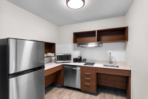 a kitchen with a stainless steel refrigerator and wooden cabinets at Everhome Suites Bastrop in Bastrop