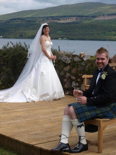 a bride and groom sitting on a bench next to the water at Rudha-na-Craige in Inveraray