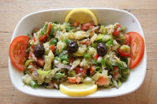 eine weiße Schüssel Salat mit Tomaten und Oliven in der Unterkunft Emel Pension in Güzelçamlı