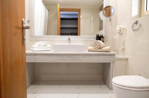 a bathroom with a sink and a toilet and a mirror at Grand Blue Beach Hotel in Kardamaina