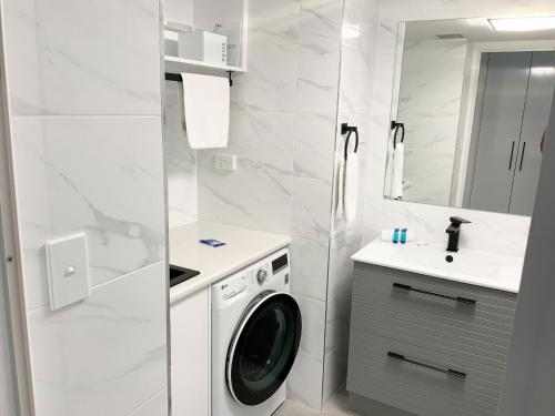 a white bathroom with a washing machine and a sink at Meridian Alex Beach Apartments in Alexandra Headland