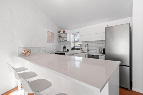a white kitchen with a white counter and a refrigerator at Sea Breeze - Orewa Oceanside Apartments in Orewa