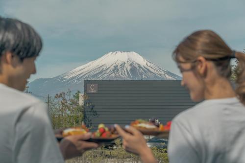 two people holding plates of food with a mountain in the background at GLANSTELLA CABIN Fujiyamanakako in Yamanakako