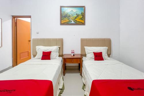 two beds in a small room with red pillows at RedDoorz at Dimens House Sragen in Sragen