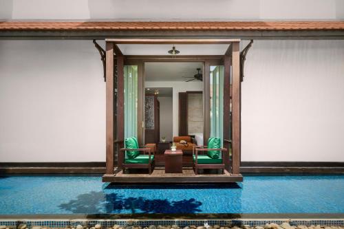 a room with chairs and a table and a pool at The Embassy Angkor Resort & Spa in Siem Reap