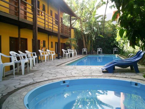 a swimming pool with white chairs next to a building at Maresias Hostel & Suites in Maresias