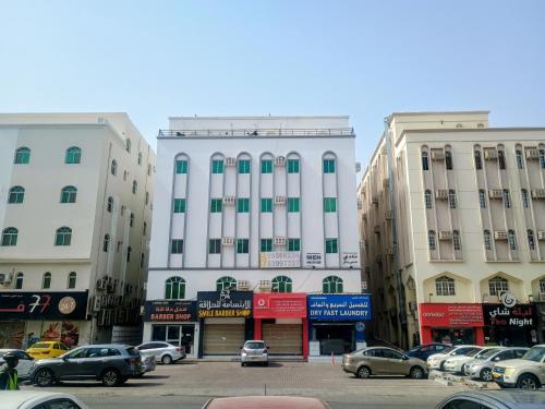 ein großes weißes Gebäude mit auf einem Parkplatz geparkten Autos in der Unterkunft Cozy Vibes Hostel in Muscat