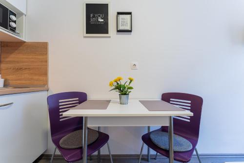 a white table with purple chairs and a vase of flowers at Flex SelfCheckIns 130 - Zagreb - Studio Apartment - Center in Zagreb