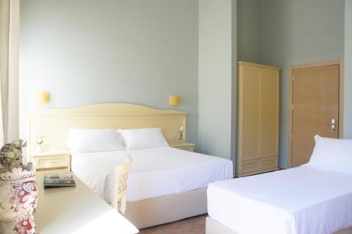 a white bedroom with two beds and a table at Hotel le Muse in Siracusa