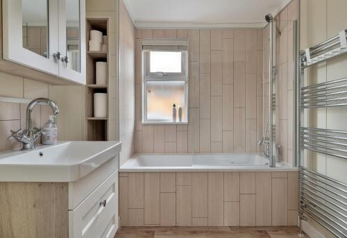 Un baño con bañera, lavabo y ventana. en Finest Retreats - Cambridge Luxury Lodge, 