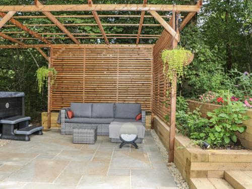 a patio with a blue couch under a wooden pergola at Charltons Hollow Cabin in Haywards Heath