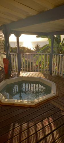 a hot tub on a wooden deck with the sun setting at Le Frégate ,belle vue mer , 150M de la plage, SPA privé in Bouillante
