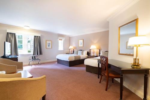 a hotel room with two beds and a desk at Orton Hall Hotel & Spa in Peterborough